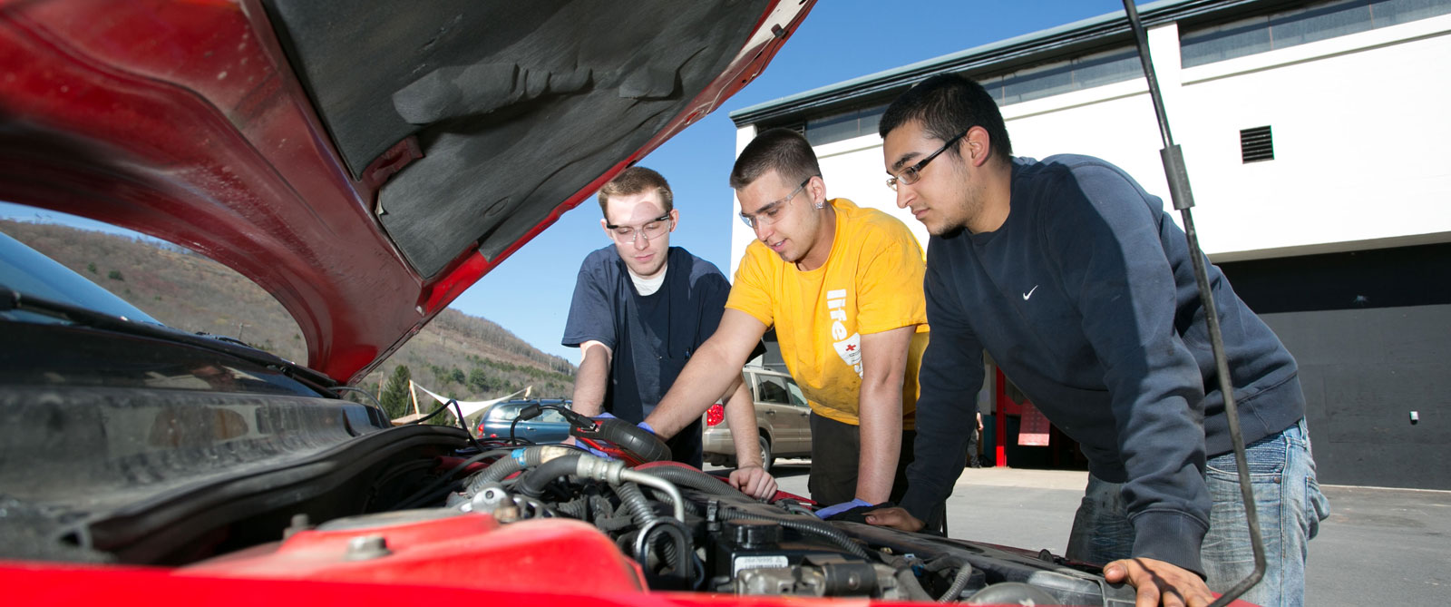 Three students working on car engine